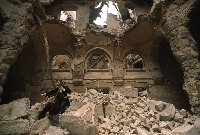 The musician Vedran Smailović plays the cello among the ruins of the National Library in Sarajevo (1992) Mikhail Evstafiev | Wikimedia Commons