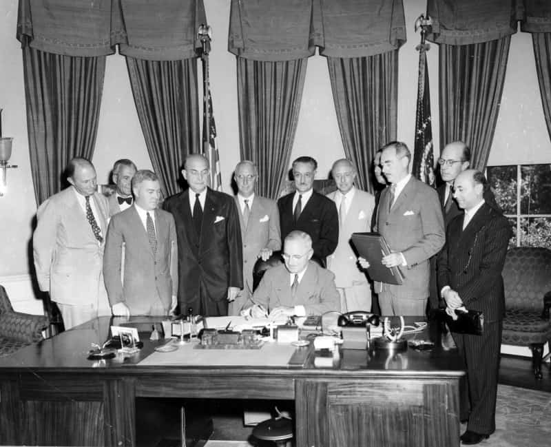 President Harry S. Truman (seated) signs a proclamation declaring into effect the 12-nation North Atlantic Pact. They are in the Oval Office. Witnessing the signing are, from left to right: Sir Frederic Hoyer-Millar of the United Kingdom; Ambassador Henrik de Kauffmann of Denmark; Canadian Embassy Counselor W. D. Matthews; Secretary of Defense Louis Johnson; Ambassador Wilhelm Munthe de Morgenstierne of Norway; Ambassador Henri Bonnet of France; Baron Robert Silvercruys, Ambassador of Belgium; Ambassador Pedro Pereira of Portugal (partly obscured by Acheson); Secretary of State Dean Acheson; Netherlands Minister Jonkheer Otto Reuchlin; and Italian Embassy Counselor Mario Lucielli | Credit: Abbie Rowe National Park Service, Harry S. Truman Library & Museum.